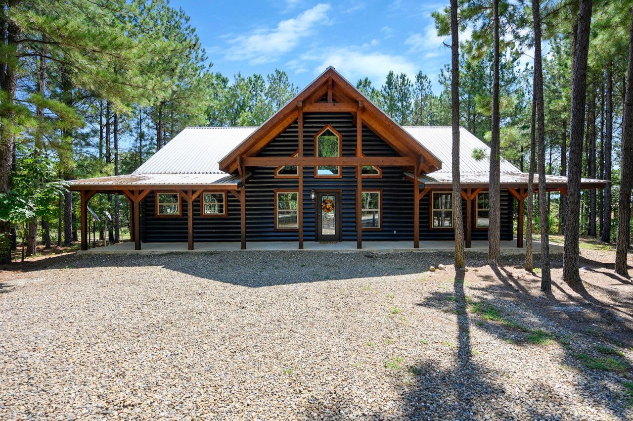 A log cabin with a gabled roof, wooden exterior, and a gravel driveway.