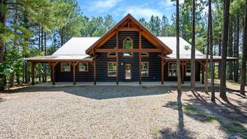 A log cabin with a gabled roof, wooden exterior, and a gravel driveway.