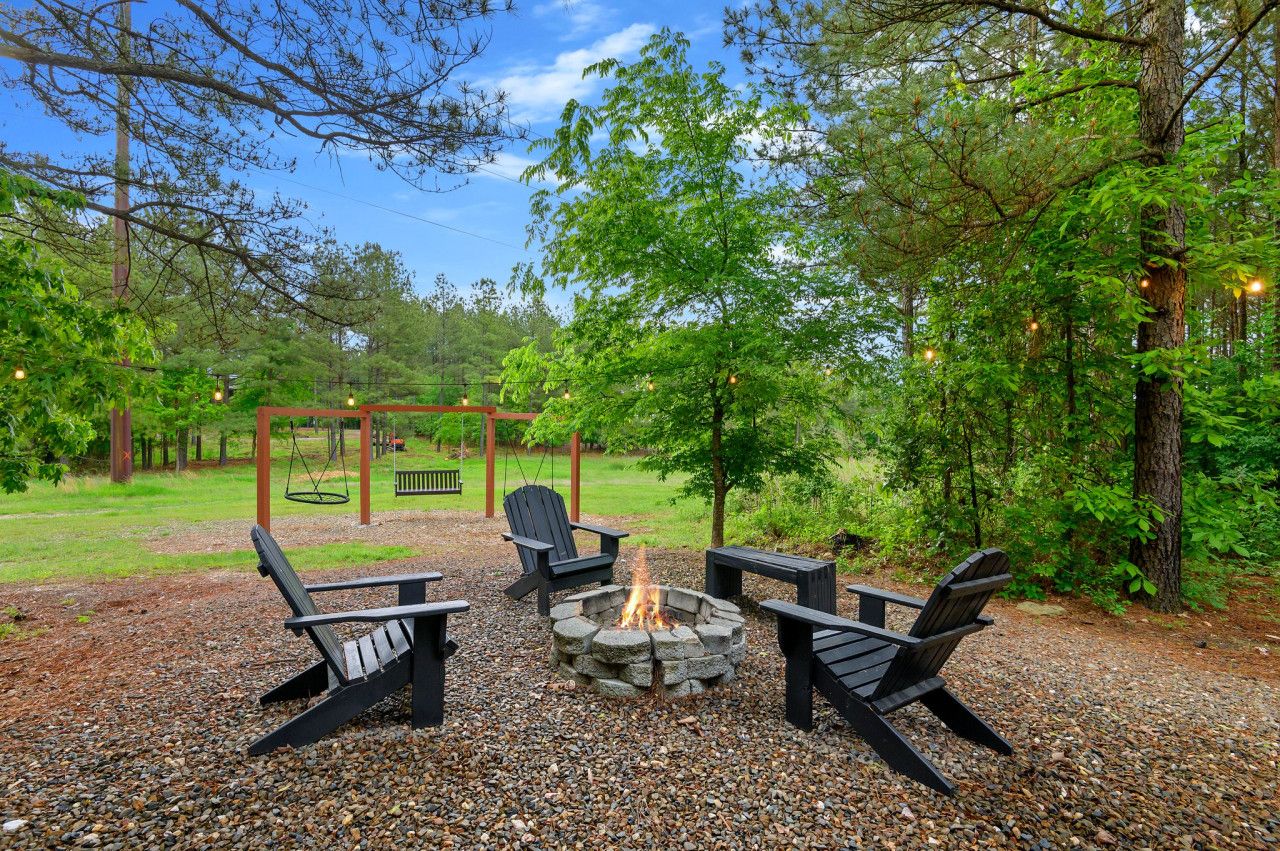 A fire pit with four Adirondack chairs, surrounded by gravel and trees.