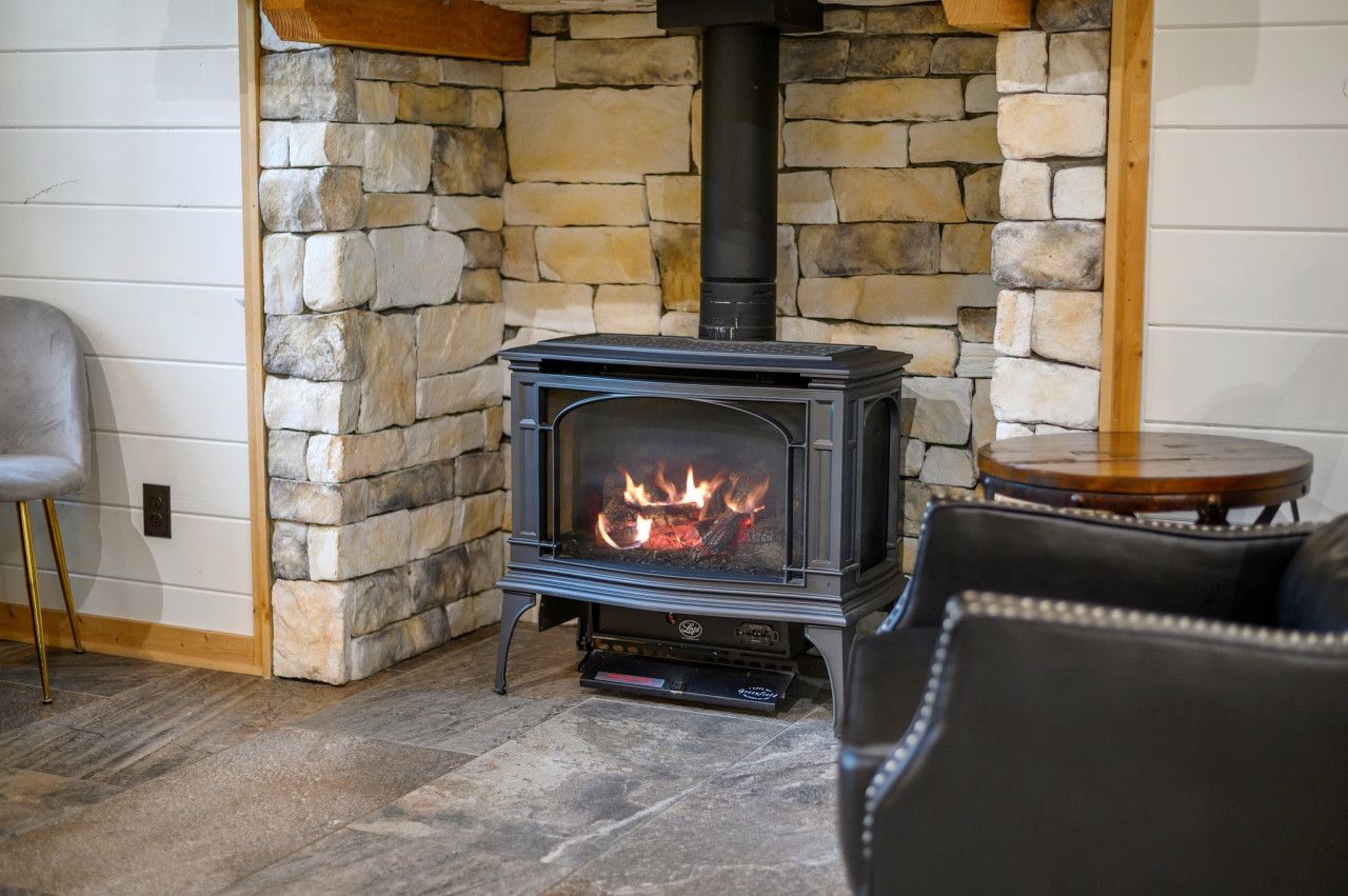 A stone fireplace with a modern wood-burning stove, a leather sofa, and a small wooden table in a cozy room.