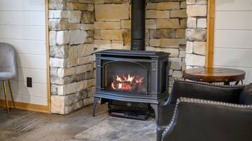 A stone fireplace with a modern wood-burning stove, a leather sofa, and a small wooden table in a cozy room.