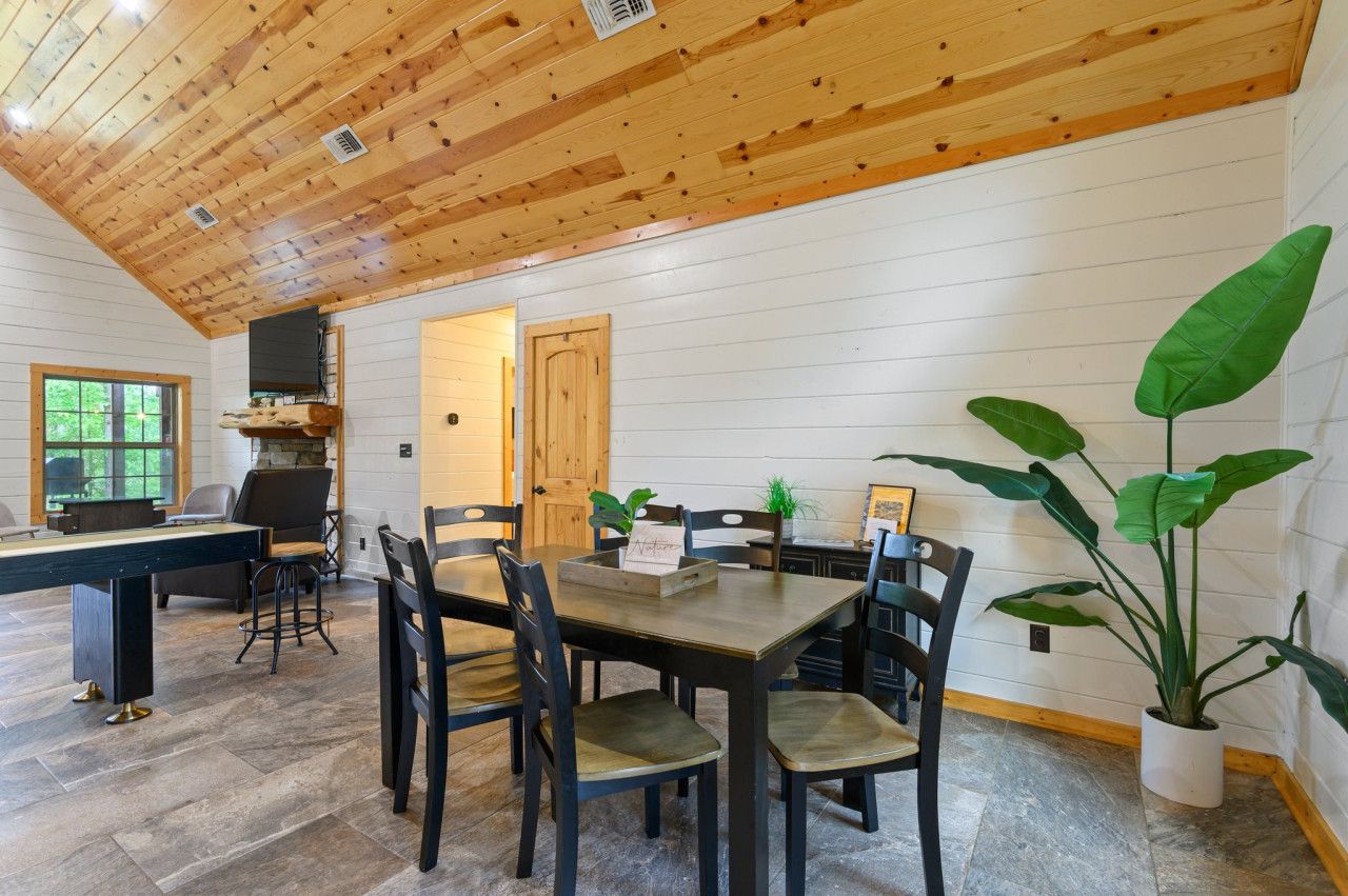 A dining area with a wooden ceiling, white walls, and a large potted plant.