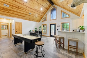 A spacious room with a pool table, bar stools, and a high ceiling with wooden beams.