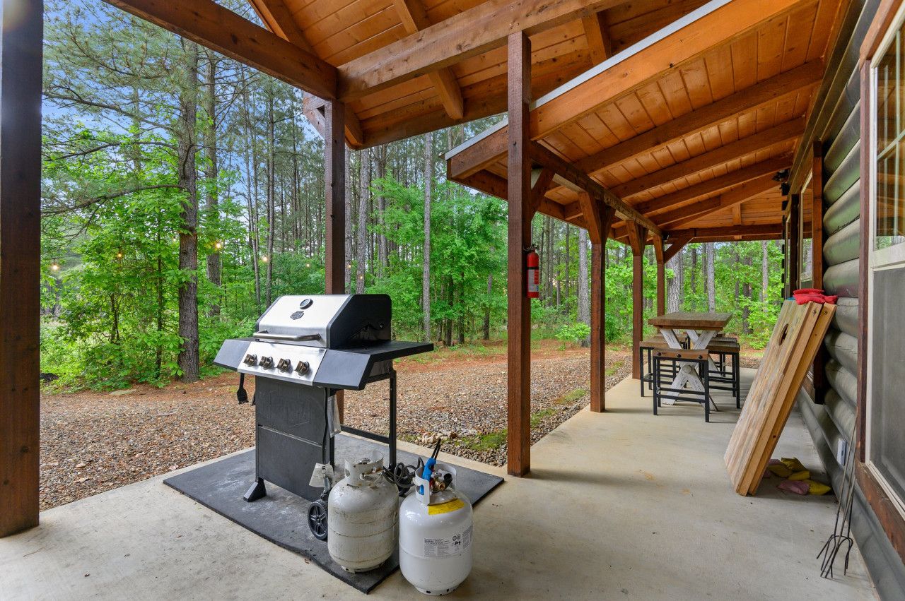 A covered outdoor area with a grill and propane tanks, surrounded by forest.