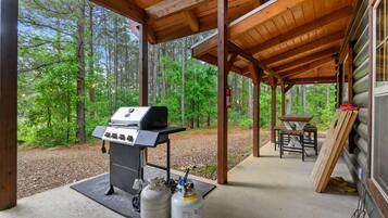 A covered outdoor area with a grill and propane tanks, surrounded by forest.