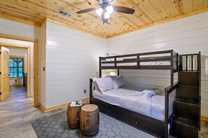 A bunk bed room with a ceiling fan, wooden walls, and a window.