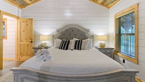 Ein Schlafzimmer mit einem großen Bett, Holzboden, weißen Wänden und einem Fenster mit Jalousien.
