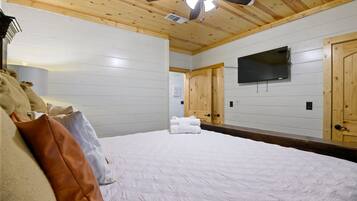 A bedroom with a bed, a ceiling fan, a mounted TV, and wooden doors.