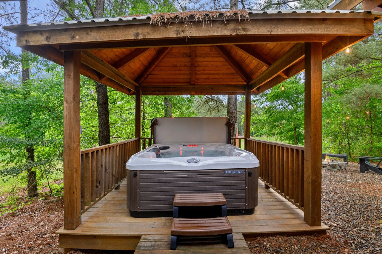 Un bain à remous installé sous une pergola en bois, entouré d’arbres.