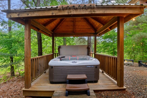 A hot tub under a wooden gazebo surrounded by trees.