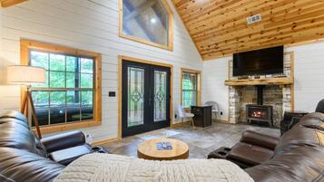 A cozy cabin interior with a stone fireplace, leather sofas, and large windows.