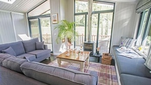 Una sala de estar acogedora con un sofá gris, una mesa de centro de madera y vistas al exterior a través de amplios ventanales.
