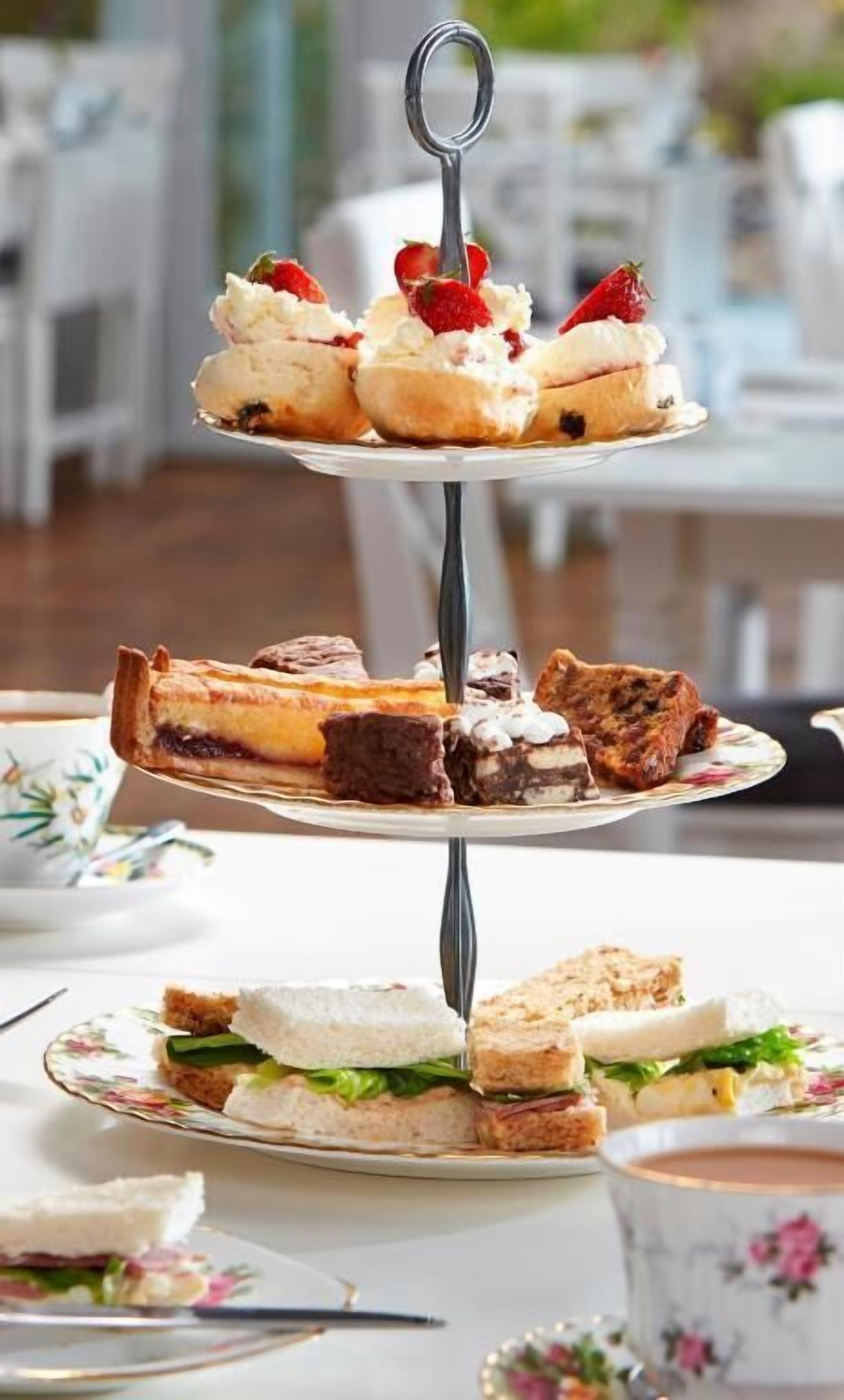 A tiered serving tray with pastries, sandwiches, and a teacup.