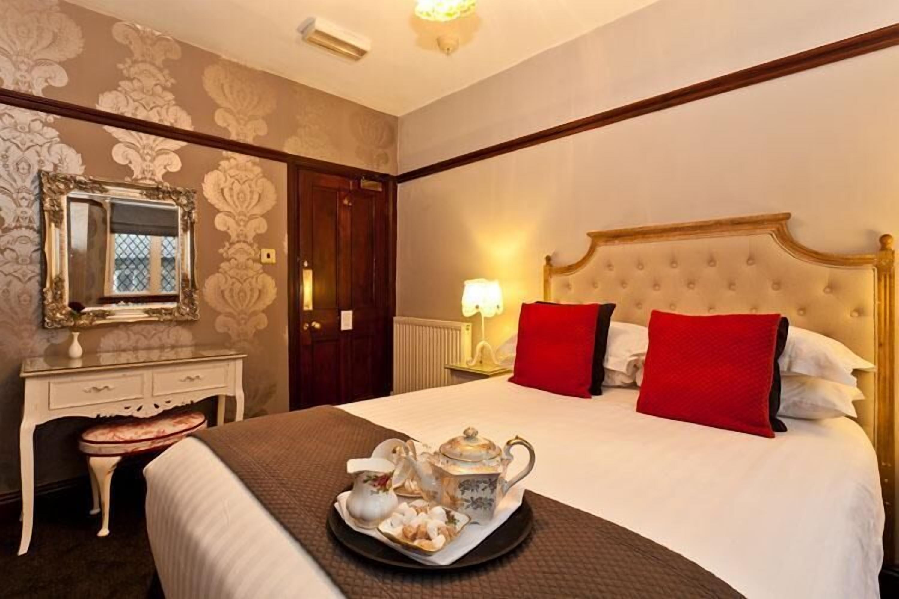 A hotel room with a large bed, a dresser, a mirror, and a tray with tea and pastries.