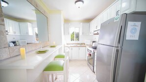 Una cocina moderna con armarios blancos, un refrigerador de acero inoxidable y una isla central con sillas verdes.
