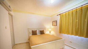 Un dormitorio con cama, mesita de noche, lámpara, ventana con cortinas y un equipo de aire acondicionado.