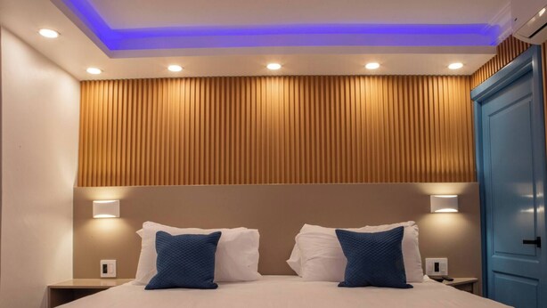 A hotel room with a bed, two bedside tables, a nightstand, a blue wardrobe, and a ceiling with recessed lighting. - Garden Condos 39, Luxury Apartment In Sosua Town! (Sosúa)