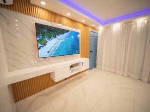 Ein modernes Wohnzimmer mit einem großen Flachbildfernseher, der an einer Wand mit marmorartigem Muster angebracht ist, einer Holzpaneel-Verkleidung und einer weißen Unterhaltungsanlage mit Schubladen.