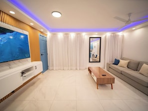 Ein modernes Wohnzimmer mit Fernseher, Couch, Holztisch und Deckenventilator.