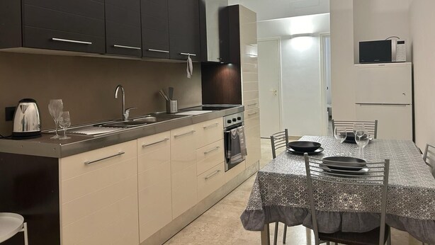 A modern kitchen with dark cabinets, a stainless steel sink, and a dining area with a patterned tablecloth. - Casa Teresa (Firenze)