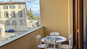 A balcony with a round table and white chairs, overlooking a street with buildings and a clear sky. - Casa Teresa (Firenze)