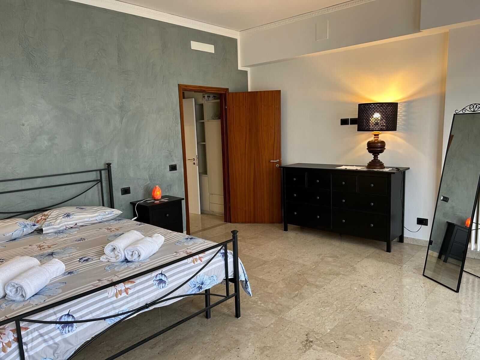 A bedroom with a bed, a nightstand, a dresser, a mirror, and a door leading to another room.