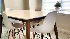 Comedor con una mesa rectangular y cuatro sillas blancas de patas de madera.