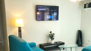 Una sala de estar moderna con un televisor de pantalla plana montado en la pared que muestra una interfaz de Roku. Hay dos sofás azules, una pequeña mesa de vidrio y una lámpara de pie.