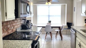 Una cocina equipada con microondas, estufa y cafetera. Hay una mesa de comedor con sillas y una ventana con vistas.