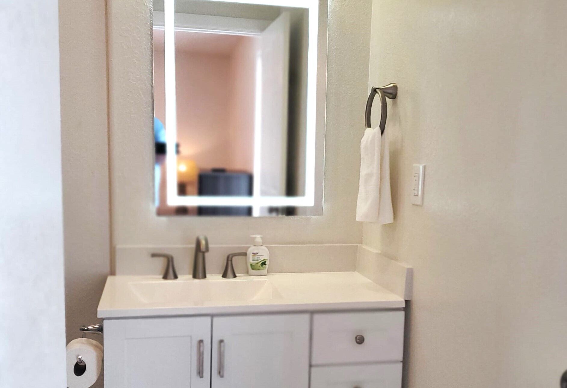 A bathroom with a white sink, two faucets, a mirror, a towel rack, and a toilet paper holder.