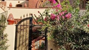 Un edificio tradicional con fachada de ladrillo, un portón decorativo y un pequeño patio con plantas y una mesa.
