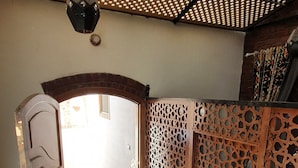 Un espacio al aire libre techado, con ventilador de techo, una puerta de madera y un muro con diseño.