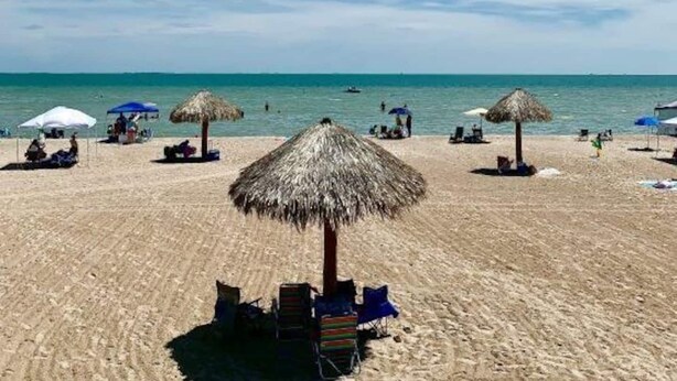 Ein Strand mit Reetsonnenstühlen und Liegestühlen, einem klaren Himmel und ruhiger See.