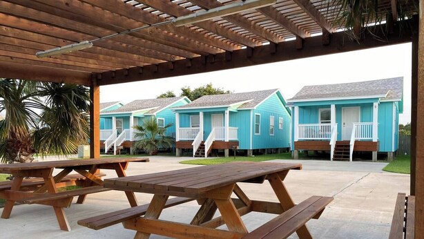 A covered outdoor area with picnic tables and a row of blue beach houses. - This house is a 2 bedroom(s), 1 bathrooms, located in Rockport, TX. (Rockport)