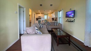 A living room with a sofa, a glass coffee table, and a TV mounted on the wall. - This house is a 2 bedroom(s), 1 bathrooms, located in Rockport, TX. (Rockport)