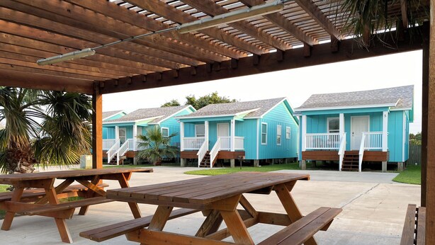 Un espacio al aire libre cubierto con mesas de picnic y una hilera de casas azules con barandillas blancas.