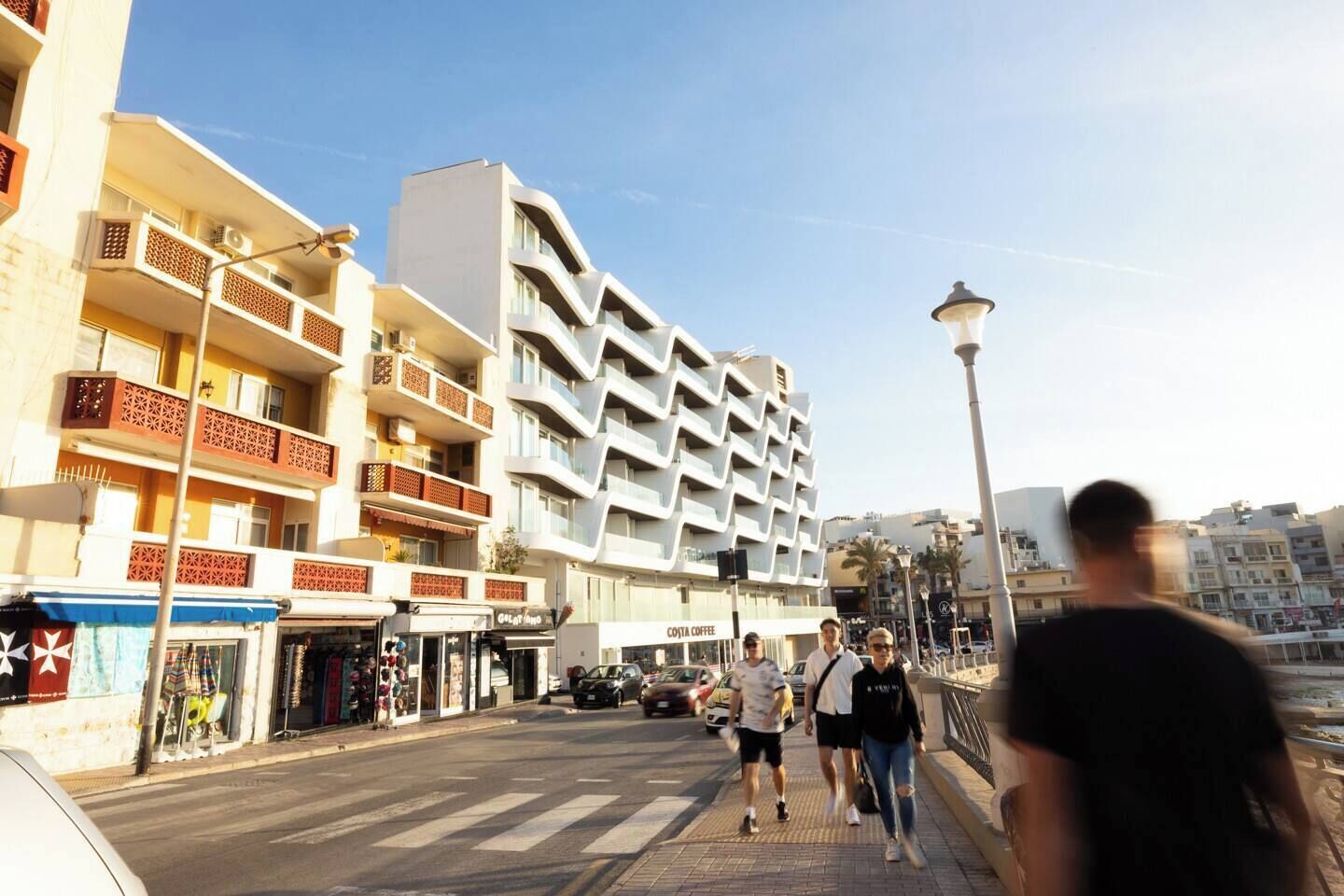 Eine Straße mit modernen Gebäuden, einer Fußgängerampel und blauem Himmel.