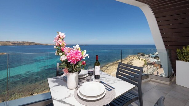 Mesa para dos con vista al mar, una botella de vino y un jarrón de flores.