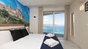 Habitación de hotel con una cama grande, vista al mar y un mural en la pared.
