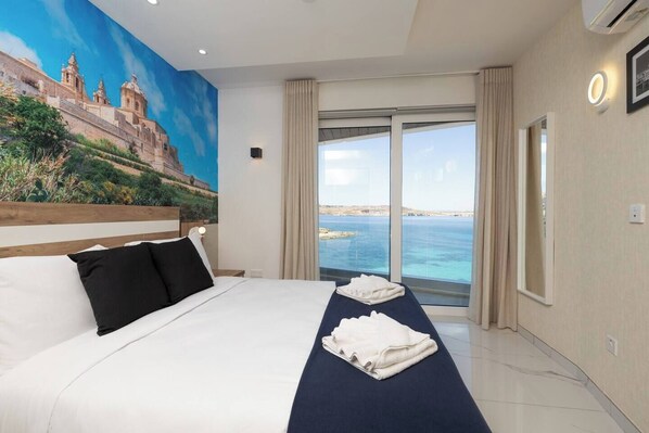 A hotel room with a large bed, a view of the sea, and a mural on the wall.