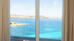 Una habitación con un ventanal grande que ofrece vistas a un paisaje costero y aguas azules cristalinas.