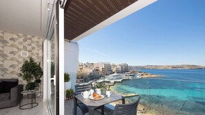 A balcony with a table set for breakfast, overlooking a coastal town and clear blue sea.