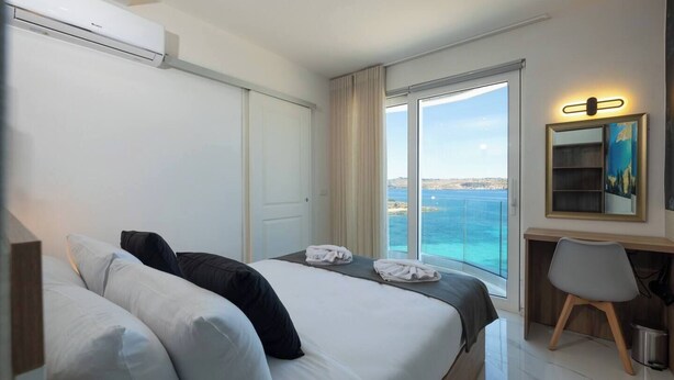 A hotel room with a large bed, a desk, and a view of the sea.