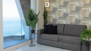 A modern living room with a grey sofa, two potted plants, and a patterned wall. - Modern seafront apartment in Bugibba Just steps from the beach, offering stylish comfort, fast WiFi, AC, and a fully equipped kitchen—perfect for a relaxing getaway (San Pawl il-Baħar)