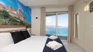 A hotel room with a large bed, a view of the sea, and a mural on the wall. - Modern seafront apartment in Bugibba Just steps from the beach, offering stylish comfort, fast WiFi, AC, and a fully equipped kitchen—perfect for a relaxing getaway (San Pawl il-Baħar)