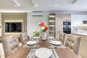 Un espace repas moderne avec une table en bois dressée pour quatre personnes, entourée de chaises rembourrées. Un vase rempli de fleurs est placé au centre.