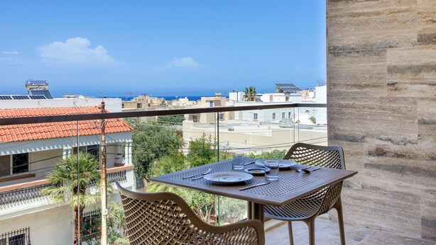 A balcony with a table set for two, overlooking a cityscape with buildings and the sea.