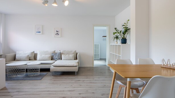 Ett modernt, minimalistiskt vardagsrum med en soffa, ett matbord och ett köksområde i bakgrunden.