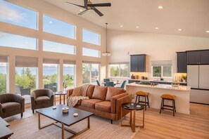 A spacious living room with a large window, a ceiling fan, and a kitchen area with a bar. - Winter King (Homer)