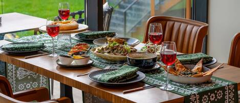 A dining table set with various dishes, glasses of red wine, and a green patterned tablecloth.
